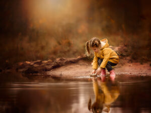 Canon Eos r6 fall image of a little girl playing with a paper boat in water wearing a yellow raincoat by Dutch photographer Willie Kers copy